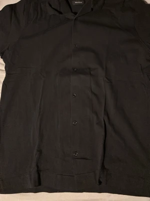 Svart skjorta från Matinique - Klassisk svart skjorta från Matinique med kort ärm och knappar framtill. Skjortan har en enkel och stilren design som passar till många olika looks. Tillverkad i mjukt material för skön känsla.