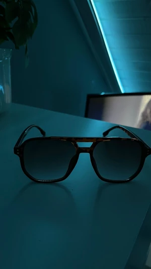 ”Grisch” solglasögon  - Snygga solglasögon med klassiska pilotbågar i brunmelerad plast och mörka tonade glas. Ramen har en cool detalj över näsryggen och glasen är stora för en trendig look. Perfekta för att lyfta din stil i sommar!