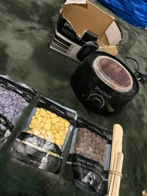 Pearlwax vaxvärmare med vaxpärlor - Komplett kit med svart Pearlwax vaxvärmare, tre påsar hårda vaxpärlor i lila, gul och brun samt träspatlar. Perfekt för smidig hårborttagning hemma. Allt du behöver för vaxning samlat i ett paket. 
