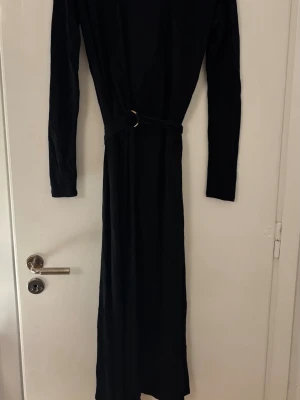 Svart långklänning från & Other Stories - Stilren svart långklänning från & Other Stories Paris Atelier med lång ärm och markerad midja med bältesdetalj. Klänningen har en enkel, elegant siluett och är perfekt för dig som gillar minimalistisk stil.