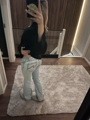 Ljusblå ripped jeans med broderad ficka - Säljer ett par ljusblå jeans med raka ben och slitningar på knäna. Jeansen har en broderad detalj på bakfickan och klassisk femficksmodell. Perfekta för en avslappnad och trendig look.