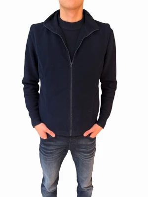 Marinblå fleeceväst med dragkedja - Marinblå väst i mjuk fleece med hög krage och hel dragkedja framtill. Västen har en enkel och stilren design utan synliga detaljer eller mönster, perfekt att slänga på sig när det är lite kyligt. Passformen är normal och materialet känns skönt mot huden.