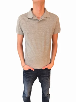 Grå pikétröja med krage - En stilren grå pikétröja med klassisk krage och korta ärmar. Perfekt till jeans eller shorts för en avslappnad look. Tröjan är tillverkad i ett mjukt material som känns skönt mot huden.