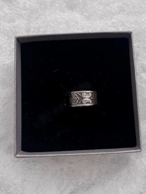 Bred silverfärgad ring med rosmönster tillverkad på återvunna bestick  - Säljer en bred ring i silverfärgad metall med detaljerat blommönster och dekorativa inslag runt hela ringen. Ringen har en bohemisk och unik känsla, perfekt för dig som gillar statement-smycken.