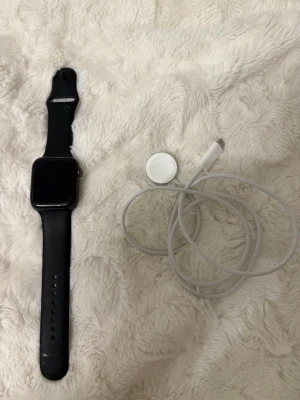 Apple Watch med svart sportband - Säljer en Apple Watch Series 5 i mycket fint skick. Det är 44 mm-modellen i Space Gray aluminium med GPS + Cellular (e-SIM), vilket gör att du kan ringa och använda appar även utan iPhone. Batterihälsan är på 94 %, vilket är ovanligt och innebär batteri i nyskick. Klockan har Always-On Retina-skärm och är vattentålig upp till 50 m. Utloggad från iCloud, nollställd och redo att användas. Svart sportarmband och laddkabel ingår.