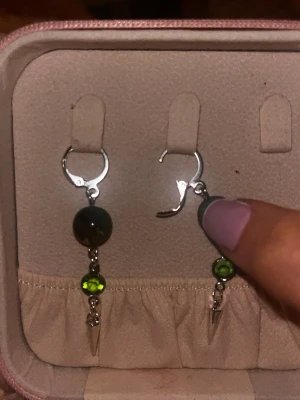 Silvriga örhängen med gröna pärlor - Snygga örhängen i silverfärgad metall med två gröna pärlor och en liten spetsig detalj längst ner. Perfekta för att ge din look lite edge och färg. Hängande modell med smidig stängning.