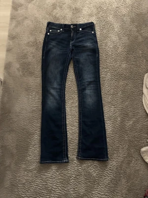 Bootcut jeans från True Religion - Mörkblå bootcut jeans från True Religion med kontrastsömmar och klassiska fickor bak. Jeansen har en snygg tvätt med slitningar framtill och silverfärgade detaljer. Perfekta för dig som gillar en tidlös och cool look. Pris kan diskuteras!💕