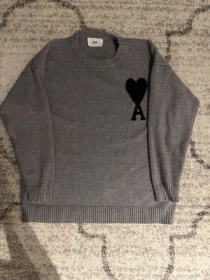 Grå stickad tröja från Ami Paris - Stilig grå stickad tröja från Ami Paris med svart hjärta. Den är i storlek L men passar M. Hör av er vid minsta fundering😁