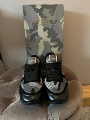 Valentino Garavani camo sneakers - Snygga sneakers från Valentino Garavani med svart, grått och vitt camouflagemönster. Skorna har svarta snören, rund tå och detaljer i både mesh och skinn. Perfekta för dig som vill sticka ut med en exklusiv och modern stil. Pris kan diskuteras 
