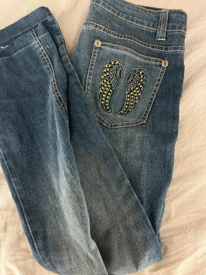 Blå jeans med vingar på bakfickor - För dig som kan sy! Säljer ett par sjukt snygga jeans. Extremt Lågmidjade och sjukt snygga. Jag har försökt att sy de i skrevet för att de skulle bli Lågmidjade. Jag kan inte sy! Så jag gav upp. Om du kan fixa dessa jeansen, kommer de att vara det snyggaste plagget du äger💗 passar S och M!