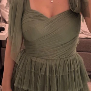 Grön långklänning med volanger - Supersöt grön långklänning med flera lager volanger och omlottliv. Klänningen har breda axelband med stora knytrosetter det är en perfekt balklänning prislappen sitter kvar  ordinarie pris: cirka 1300 mitt pris:950( pris kan diskuteras)