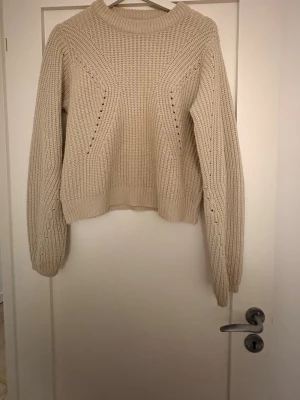 Beige stickad tröja med vida ärmar - Mysig beige stickad tröja med rund hals och vida, långa ärmar. Tröjan har en ribbad struktur och avslappnad passform, perfekt för lager-på-lager och en chill stil.