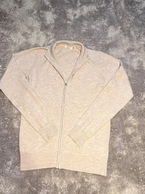 Beige ziptröja från RYVLS  - Snygg beige ziptröja från RYVLS med hög krage och långa ärmar. Tröjan har ribbade muddar vid ärmslut och nederkant samt dragkedja framtill. Perfekt för lager på lager och enkel att matcha med olika outfits. DENNA TRÖJA ÄR HELT NY ALDRIG ANDVÄNDS!! NYPRIS 599kr