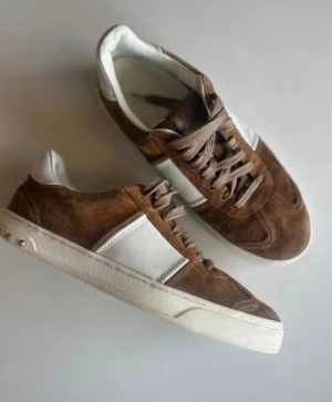 Valentino Garavani Flycrew sneakers, brun mocka/vitt läder -  Exklusiva Flycrew sneakers från Valentino Garavani i brun mocka med vita läderdetaljer. Stilrena, bekväma och tidlösa – passar både till jeans och mer dressade outfits. 	•	Storlek: 41 	•	Färg: Brun / Vit 	•	Material: Mocka & läder 	•	Skick: Använda, i fint skick! anmärkning är att en nit lossnat. Lite nött undertill mot hälar. (Se närbilder) 	•	Nypris: ca 7 500kr