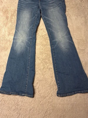 Blå bootcut jeans med utsvängda ben - Snygga blå jeans med bootcut-modell och utsvängda ben. Jeansen har klassisk femficksdesign och ljusa slitningar framtill för en cool, avslappnad look. De har använts få gånger 