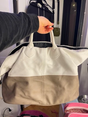 Beige och vit resväska från Pieces - Snygg tvåfärgad resväska från Pieces i beige och vitt. Väskan har dubbla handtag, dragkedja upptill och är tillverkad i ett slitstarkt syntetmaterial med struktur. Perfekt för weekendresor eller som gymväska.