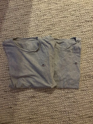 Grå t-shirt från Gant med logga - Säljer en klassisk grå t-shirt från Gant med rund hals och liten broderad logga på bröstet. T-shirten är enkel och stilren, perfekt till jeans eller shorts. Tillverkad i mjuk bomull för skön känsla och den passar en person mellan 155-165 cm 