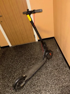Svart elscooter med laddare - Säljer en svart elscooter med grå handtag och röda detaljer. Scootern har en robust ram i metall och medföljer gör en laddare. Perfekt för att ta sig runt i stan på ett smidigt sätt. Stänkskydd bak och halkfri platta för fötterna.
