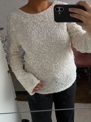 Vit paljettopp med öppen rygg - Säljer en glittrig vit topp med paljetter och lång ärm. Toppen har en snygg öppen rygg och rund halsringning framtill. Använd 1 gång. Jätte lite smink vid halsringningen insidan av tröjan som knappt syns (se bild), men vill informera ändå. Går bort vid tvätt 🫶🏼