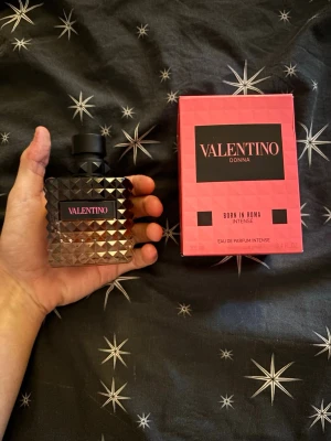 Valentino Donna Born In Roma Intense - Lyxig parfym från Valentino, Donna Born In Roma Intense. Flaskan är fyrkantig med nitar i glaset och svart lock. Förpackningen är rosa med svarta detaljer och tydlig logga. Eau de Parfum Intense för en djärv och elegant doft.