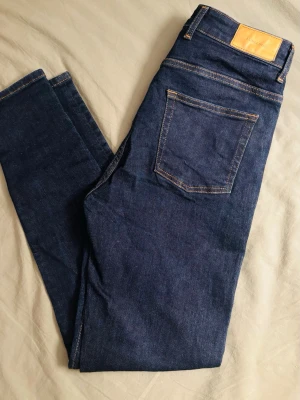 Mörkblå jeans från J.Lindeberg - Snygga mörkblå jeans från J.Lindeberg med klassisk femficksdesign och kontrastsömmar. Jeansen har en rak passform och är tillverkade i slitstarkt denimtyg av bomull. Perfekta för dig som gillar stilrena och tidlösa jeans.