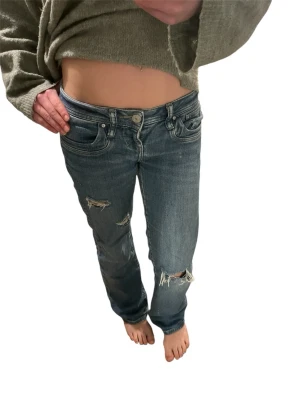 Blå slitna jeans från LTB - Säljer ett par blå jeans från LTB med slitna detaljer och hål på benen. Jeansen har klassisk femficksmodell, låg midja och bootcut ben. Perfekta för en avslappnad och trendig look. Storlek 24/30