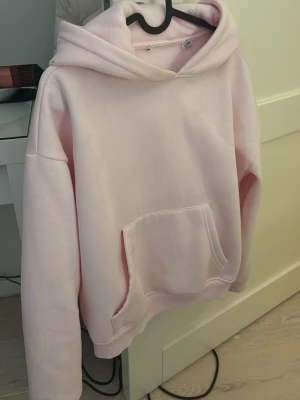 Ljusrosa hoodie med magficka - Säljer en oversized ljusrosa hoodie med stor huva och rymlig magficka. Hoodien har ribbade muddar vid ärmslut och nederkant, samt en clean look utan tryck eller logga. Perfekt för dig som gillar en enkel och chill stil.