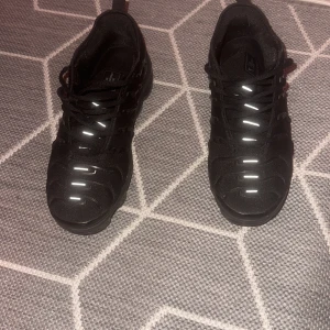 Nike Air Vapormax svarta sneakers - Svarta Nike Air Vapormax sneakers med reflekterande detaljer på ovandelen och unik bubblig sula. Skorna har snörning och en sportig, futuristisk look. Ovandelen är i syntet och mesh för bra andningsförmåga. Perfekta för dig som gillar streetwear och vill sticka ut.