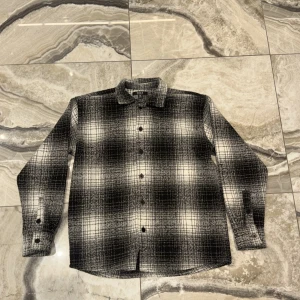 Oversized rutig skjorta från Smog - Säljer en oversized rutig skjorta från Smog i svart och vitt. Skjortan har klassisk krage, knäppning framtill och långa ärmar med manschett. Perfekt för dig som gillar en loose och avslappnad stil.