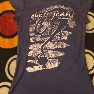 Blå t-shirt Guess Jeans Los Angeles - Snygg blå t-shirt från Guess Jeans Los Angeles med coolt vitt tryck framtill. T-shirten har korta ärmar och är gjord i mjuk polyester med lite stretch för skön passform. Perfekt för dig som gillar streetstyle och vill sticka ut med ett unikt print.