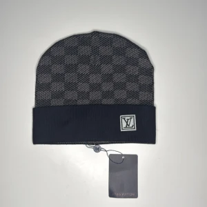 Lv mössa grå/svart - Snygg mössa från Louis Vuitton i grått och svart med diskret rutigt mönster och vikt kant. LV-logga framtill på kanten. Perfekt accessoar för att hålla stilen kallare dagar.