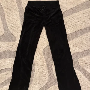 Svarta velourbyxor Juicy Couture S - Svarta mjukisbyxor från Juicy Couture i mjuk velour med bred resår och snörning i midjan. Byxorna har raka ben, två fickor fram och diskret JC-logga på ena fickan. Perfekta för en chill och trendig look. Saknas en metallbit på ena knytsnöret men annars som nya. 