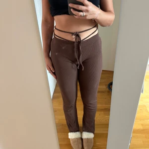 Bruna ribbade byxor med snörning från Missäy - Snygga bruna ribbade byxor från Missäy i mjukt bomullsmaterial med stretch. De har hög midja och cool snörning som går runt midjan. Passformen är tight och de är perfekta för en trendig look. Materialet är 95% bomull och 5% elastan. Klippt och sytt om så dom är lågmidajde och så dom är lite längre i benen 
