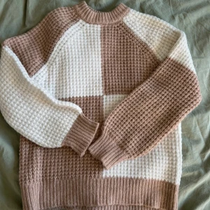 Beige och vit stickad tröja MNG XS - Säljer en chunky stickad tröja från MNG i storlek XS. Tröjan har ett rutigt mönster i beige och vitt, grovstickad struktur och ribbade muddar vid hals, ärmslut och nederkant. Perfekt för dig som gillar mysiga och trendiga plagg med lite oversized känsla.