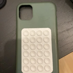 iPhone 11 Skal med Pop It Fidget - Grönt skal till iPhone 11 med integrerad vit Pop It fidget-leksak på baksidan. Skalets skick är begagnat med synligt slitage och mindre smutsfläckar. Passar perfekt för dig som vill skydda din mobil och samtidigt ha något att pyssla med.