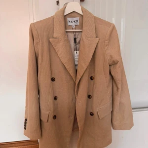 Dubbelknäppt blazer - Beige/sandfärgad dubbelknäppt manchesterkavaj från NAKD, aldrig använd med prislappen kvar. Storlek 32, dock stor i storleken kan troligen passa en storlek 34/36 också.