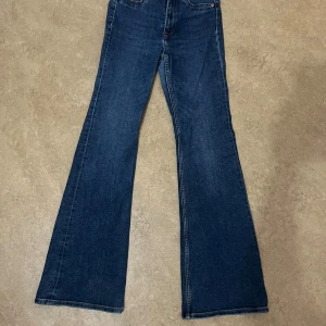Blå bootcut jeans i storlek 34 - Snygga blå bootcut jeans i klassisk modell med utsvängda ben och normal midja. Jeansen har fem fickor och är tillverkade i ett mjukt denimtyg som sitter skönt. Perfekta för dig som gillar en retroinspirerad look.