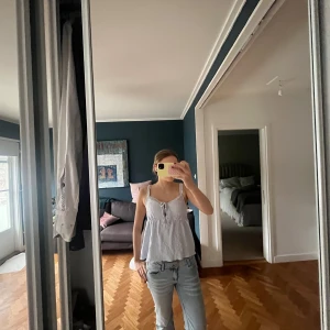 Vit spetsig linnetopp från Gina Tricot - Supersöt vit linnetopp från Gina Tricot med spetsdetaljer och knyt framtill. Toppen har smala axelband och en luftig, flowy passform. Perfekt för varma dagar och ger en romantisk vibe till din outfit.