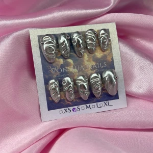 SilverChrome(S);Short Almond;Curved - Handgjorda press-on naglar i metallic chrome silver med unik 3D-effekt och små stenar. Naglarna har en cool, skulpterad yta och kommer i  S: 15 mm, 11,5 mm, 12 mm, 11 mm, 9 mm . Perfekt för dig som vill sticka ut med ett futuristiskt och edgy nagelset.