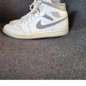 Nike Air Jordan 1 Mid  - Mid neutral Vintage grey 554724-135 sneakers i vitt och ljusgrått med klassisk Jordan-logga på sidan. Snygga och i gott skick. Storlek 45 men är små, drar 43.5 i storlek och sitter perfekt. Inköpta på Nike I Malls of Scandinavia.