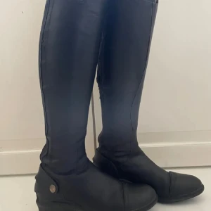 Läderridstövlar  - Läderridstövlar   Säljer dessa släta, svarta ridstövlar i storlek 37 dam. Utsidan är 100% läder och fodret är meshmaterial.  Köpta från Horze.se. Modellen heter Geneve, original pris 2790 kr.   Vissa tecken på användning, se sista bilderna.  Kan mötas upp i Stockholm annars kan jag posta. Hör av er vid fler frågor!