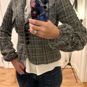 Rutig kavaj från Sisley - Säljer en snygg rutig kavaj från Sisley i svart, grått och vitt. Jackan har markerad krage, knappar framtill och puffiga långärmar. Materialet är grovt vävt och ger en cool, strukturerad look. Perfekt för dig som gillar att sticka ut med din stil.