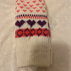 Stickade vantar med hjärtmönster - Två par stickade vantar, ett par i vitt med lila och rosa detaljer och ett par i ljusblått med svart och vitt mönster. Båda har hjärtan och små mönster över hela vanten. Perfekta för kalla dagar och riktigt mysiga att bära.   69kr/par