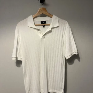 Piké/ skjorta - Helt ny, oanvänd vit kortärmad skjorta från H&M i slim fit med ribbad struktur och klassisk krage. Skjortan har knappar framtill och är gjord i mjukt bomullsmaterial. Perfekt för dig som gillar stilren och enkel design med lite extra detaljer.