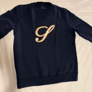 Mörkblå sweatshirt/collegetröja från Stenströms - Snygg mörkblå sweatshirt från Stenströms med ett stort broderat S i gult och vitt på bröstet. Tröjan är i 100% bomull, har rund hals och långa ärmar. Perfekt för dig som gillar stilrena detaljer och klassisk design. Endast använd ett fåtal gånger, har blivit för tjock.. 