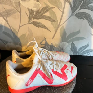 Puma vita och rosa fotbollsskor - Säljer ett par snygga fotbollsskor från Puma i vitt med starka rosa detaljer och sula. Skorna är knappt använda så de är i fint skick.