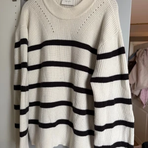 Randig stickad tröja från Neo Noir - Säljer en oversized stickad tröja från Neo Noir i vit med svarta ränder. Tröjan har rund hals, grov ribbstickning och långa ärmar.