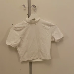 Vit croppad polotopp med kort ärm - Säljer en stilren vit polotopp med korta ärmar och croppad passform. Toppen har en enkel design med hög krage och är gjord i mjukt, hög kvalitativt bomullsmaterial. Perfekt för dig som gillar minimalistiska och fräscha plagg.