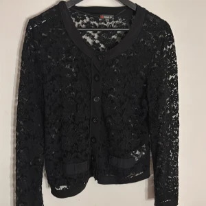 Svart spetskofta från Street One - Svart kofta i spets från Street One, med blommigt mönster och knappar framtill. Koftan har långärmade ärmar och rundad halsringning. Snygga detaljer med spets och dekorativa fickor framtill. Pris kan diskuteras💗