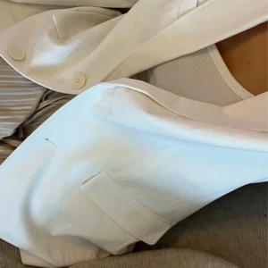 Vit kavaj från NA-KD - Snygg vit overaized kavaj från NA-KD med klassisk krage och två knappar framtill. Xs i storlek men jag själv är en S/M och den passar perfekt. Har suttit länge i garderoben o är därför skrynklig. Inget som ni kommer få med eller vara kvar. Kavajen har två fickor med lock och en rak, lite loose passform. Materialet känns mjukt och har en lätt struktur, perfekt för att lyfta din look. Taggen sitter kvar så är helt ny och oanvänd. 